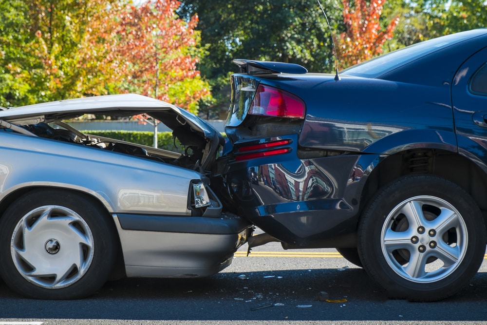 Severe rear-end collision damage to two vehicles after motor vehicle accident showing crumpled trunk and hood in New York
